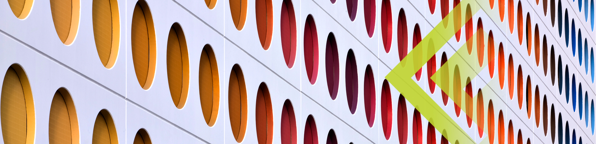 an abstract image showing the side of a silver building with an interesting design created by different coloured circles carved into the wall